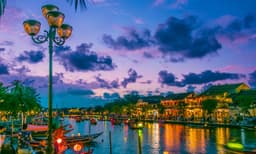 A vibrant view of Hoi An's lantern-lit riverside during dusk, with boats floating on the water and illuminated buildings reflecting in the canal.